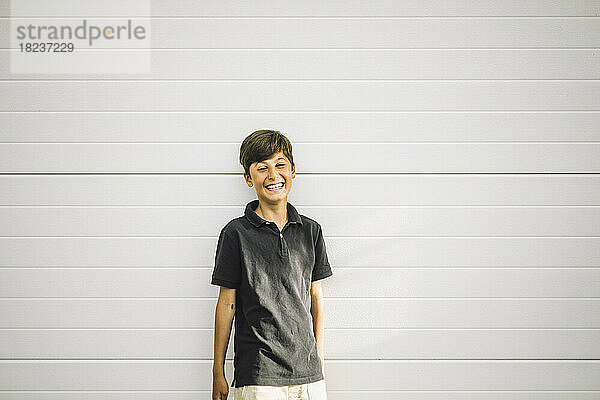 Porträt eines glücklichen Jungen  der an einer weißen Wand steht