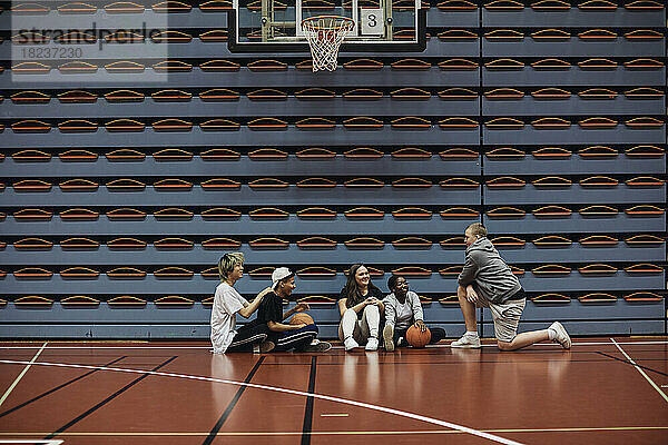 Lächelnde Jungen und Mädchen  die sich auf dem Basketballplatz in der Schule miteinander unterhalten