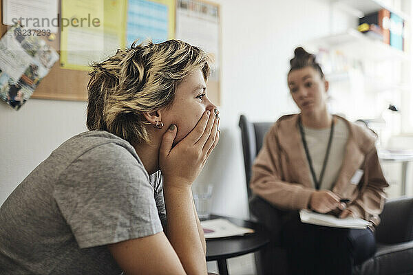 Drückt eine Schülerin  die den Mund mit der Hand bedeckt und in der Nähe des Beraters im Schulbüro sitzt