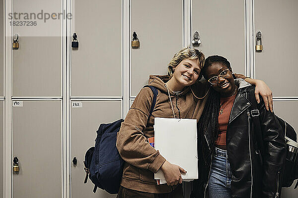 Porträt von lächelnden Freundinnen  die zusammen vor einem Spind in der Schule stehen