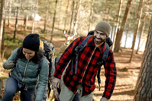 Glücklicher Mann mit kariertem Hemd beim Wandern mit einer Freundin im Wald