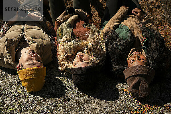 Männliche und weibliche Freunde mit Strickmütze  die sich an einem sonnigen Tag auf einem Felsen ausruhen
