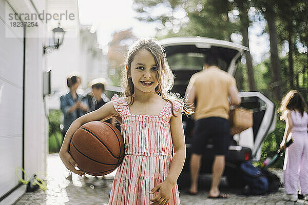 Porträt eines lächelnden Mädchens mit Basketball und Familie im Hintergrund