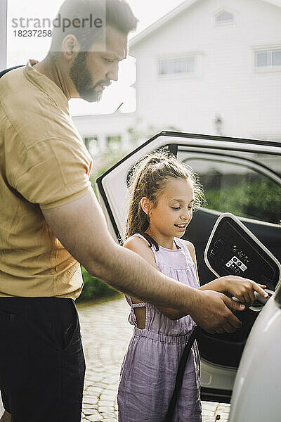 Mädchen lernt an der Seite ihres Vaters  wie man ein Elektroauto auflädt