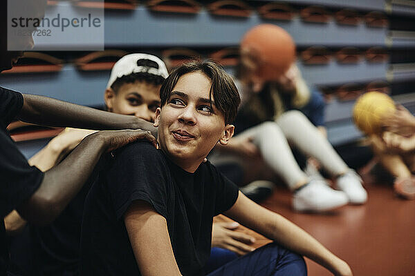 Lächelnder Teenager  der einen männlichen Freund auf dem Basketballplatz ansieht