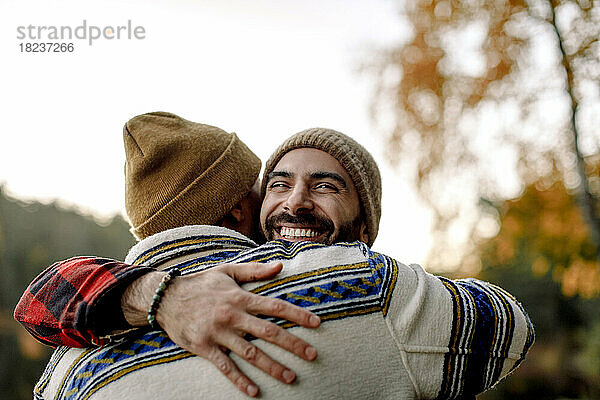 Junger Mann umarmt glücklichen männlichen Freund mit Strickmütze