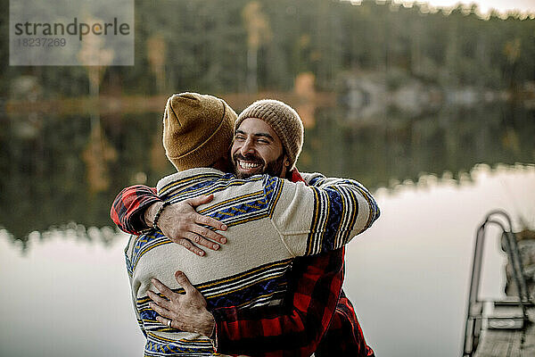 Rückansicht eines Mannes  der einen männlichen Freund in der Nähe eines Sees umarmt
