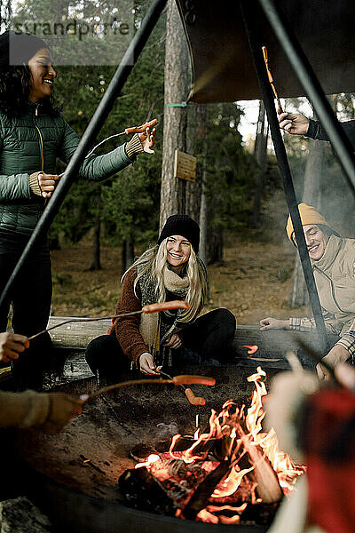 Glücklicher Mann und Freunde genießen das Essen am Lagerfeuer im Wald