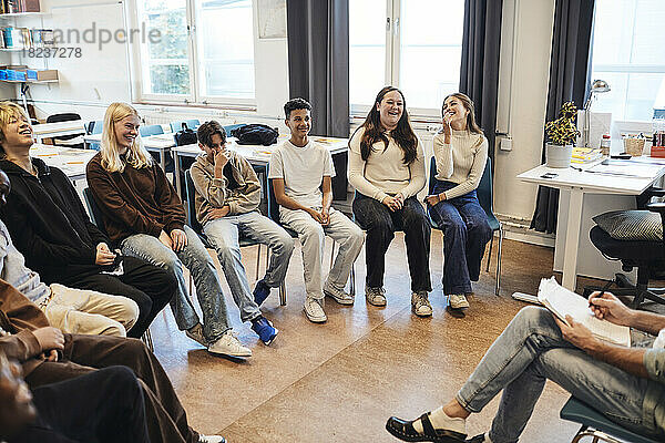 Glückliche Schülerinnen und Schüler sitzen mit einem Berater in einer Gruppentherapie in der Schule