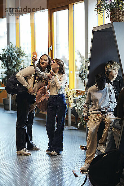 Lächelndes Teenager-Mädchen  das ein Selfie über ein Smartphone mit einer Freundin in der Schule macht