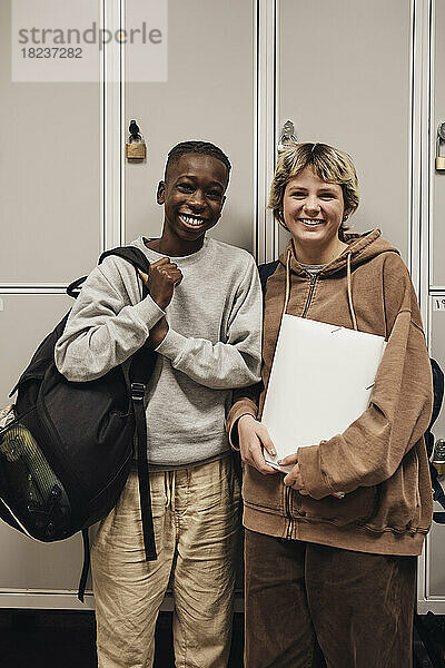 Porträt eines glücklichen Teenagers und eines Mädchens  die vor einem Spind in der Schule stehen