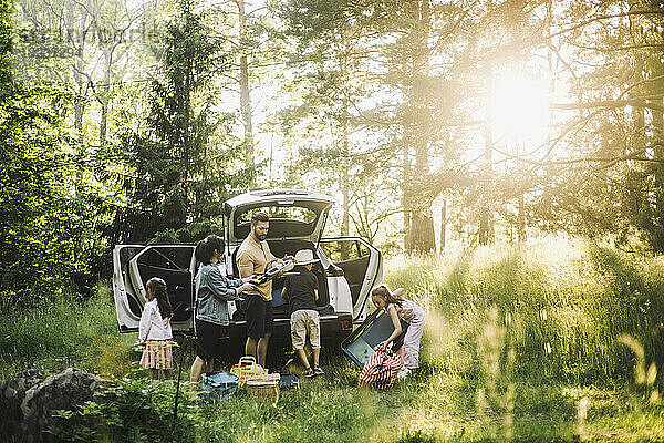 Familie entlädt Sachen aus dem Kofferraum eines Autos im Wald an einem sonnigen Tag