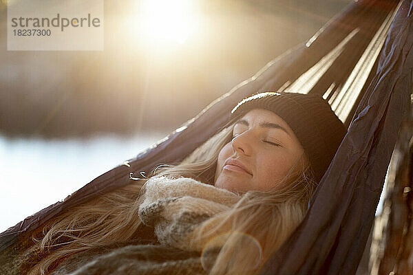 Junge Frau mit geschlossenen Augen entspannt sich in der Hängematte an einem sonnigen Tag