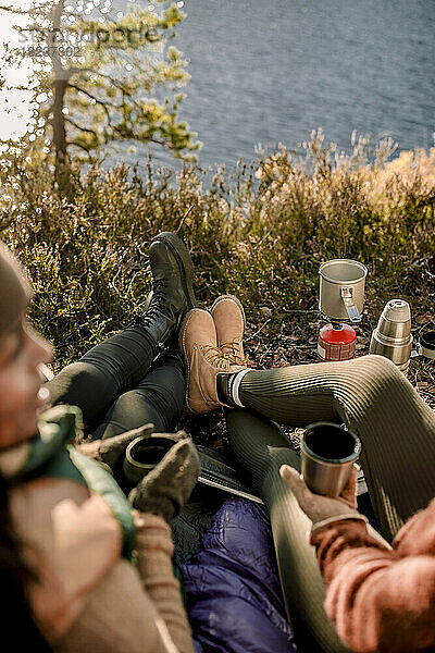 Hochformatige Ansicht von Freunden  die Stiefel tragen  während sie beim Zelten im Gras sitzen