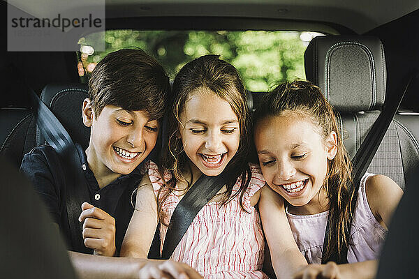 Glückliche männliche und weibliche Geschwister  die den Sicherheitsgurt tragen  während sie sich im Auto vergnügen