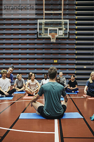 Männlicher Trainer  der männlichen und weiblichen Schülern auf dem Sportplatz Yoga beibringt