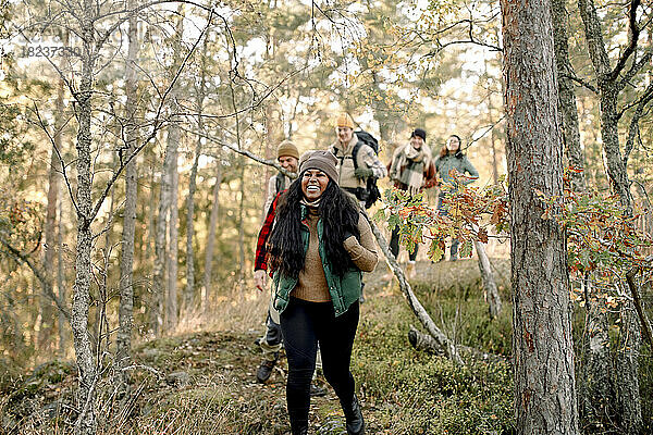 Glückliche männliche und weibliche Freunde wandern zusammen inmitten von Bäumen im Wald