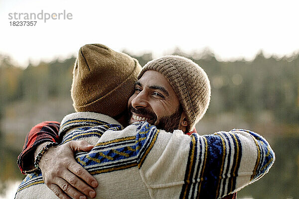 Glückliche männliche Freunde  die sich gegenseitig umarmen und Strickmützen tragen
