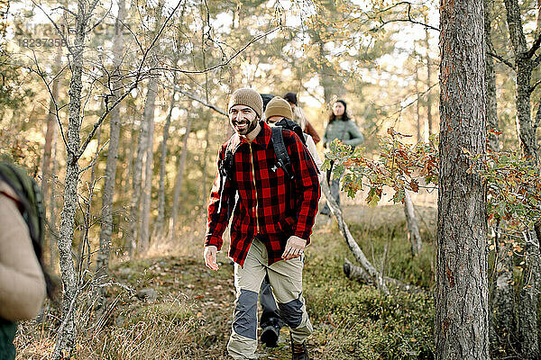 Lächelnder Mann beim Wandern mit Freunden inmitten von Bäumen im Wald