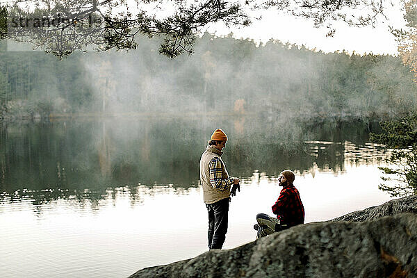 Männliche Freunde unterhalten sich auf einem Felsen in der Nähe eines Sees während eines Urlaubs