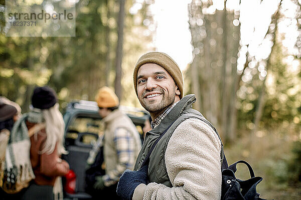 Lächelnder Mann in warmer Kleidung  der im Wald nachdenkt