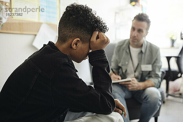 Trauriger Teenager  der bei einem männlichen Berater sitzt und im Schulbüro diskutiert