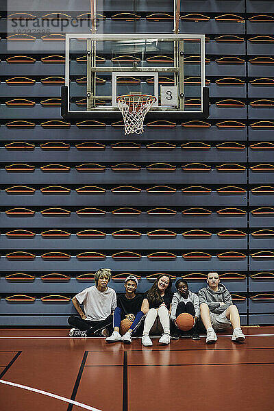 Porträt von Jungen und Mädchen in voller Länge  die zusammen auf einem Basketballplatz sitzen
