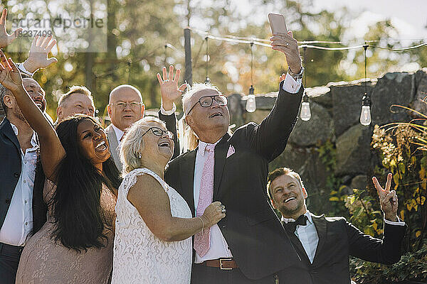 Glückliche frisch verheiratetes älteres Paar nimmt Selfie mit Familie und Freunden durch Smartphone