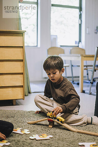 Junge spielt mit Spielzeugeisenbahn  während er auf dem Teppich im Kindergarten sitzt