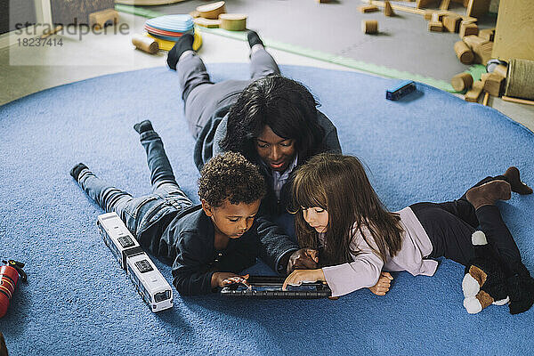 Lehrerin verwendet digitales Tablet mit Schülern in einer Kindertagesstätte