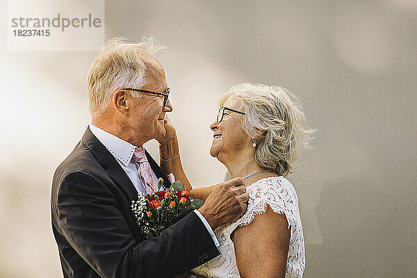 Seitenansicht eines lächelnden älteren Paares  das sich gegenseitig anschaut und an der Wand steht