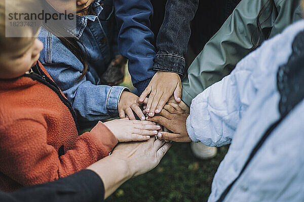 Verspielte multirassische Vorschüler stapeln Hände mit Lehrer im Park
