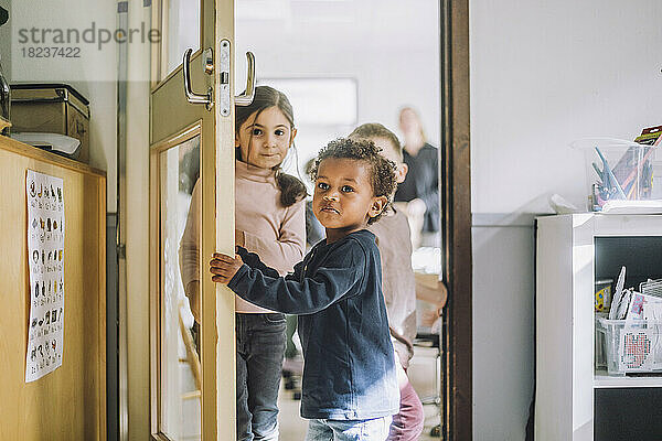 Junge  der die Tür öffnet  während er mit seinen Klassenkameraden vor der Tür des Kindergartens steht