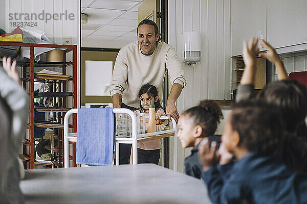 Glückliche Lehrerin und Mädchen mit Essenswagen von Mitschülern beim Frühstück in der Kindertagesstätte