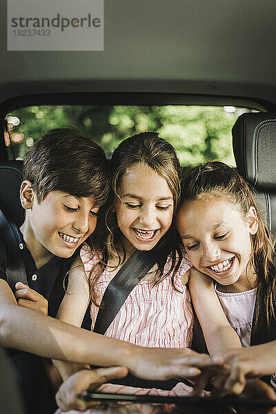 Glückliche Geschwister teilen sich einen Tablet-PC während einer Autofahrt