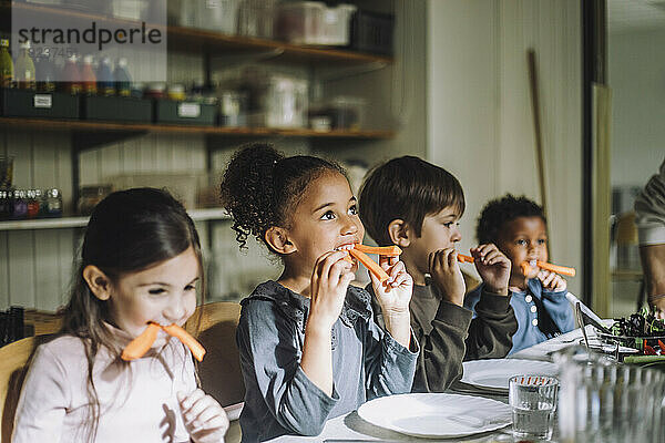 Gemischtrassige Kinder essen Karotten zum Frühstück in der Kindertagesstätte