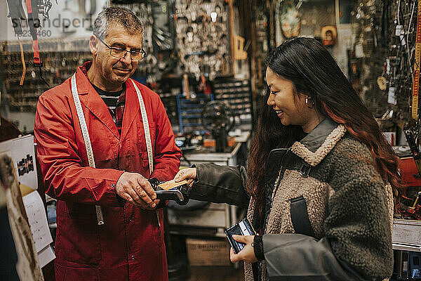 Lächelnde junge Kundin beim kontaktlosen Bezahlen mit Kreditkarte in einer Werkstatt