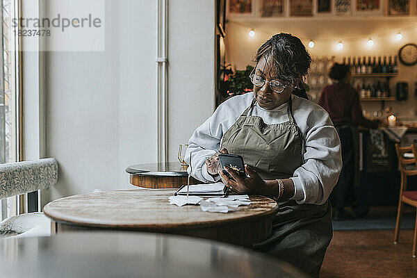 Ältere Frau  die ein Mobiltelefon benutzt  während sie mit einem Tagebuch am Tisch eines Cafés sitzt