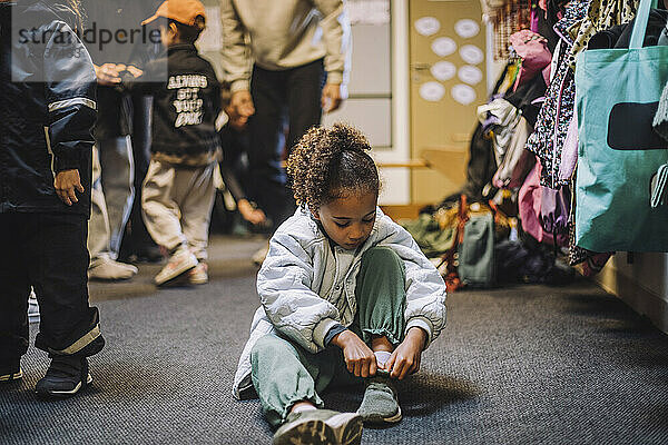Mädchen trägt Schuh  während sie auf dem Teppich in der Kindertagesstätte sitzt