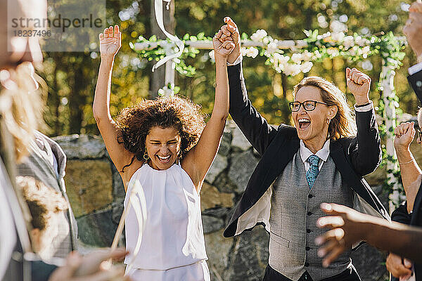 Glückliches lesbisches Paar hält sich an den Händen und tanzt inmitten von Familie und Freunden während der Hochzeitsfeier