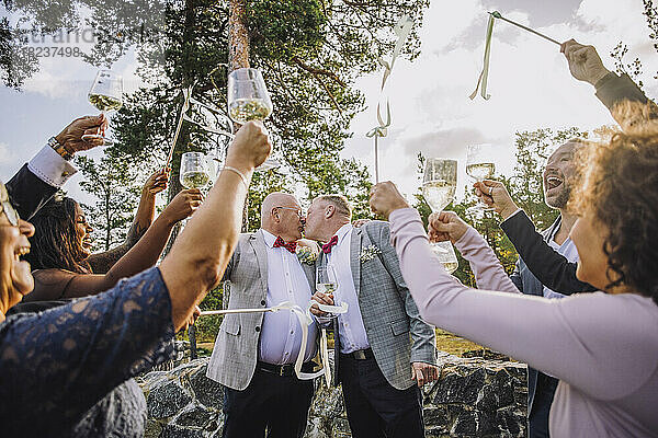 Neuvermähltes homosexuelles Paar  das sich küsst  während Freunde und Familie ihnen bei der Hochzeit zujubeln