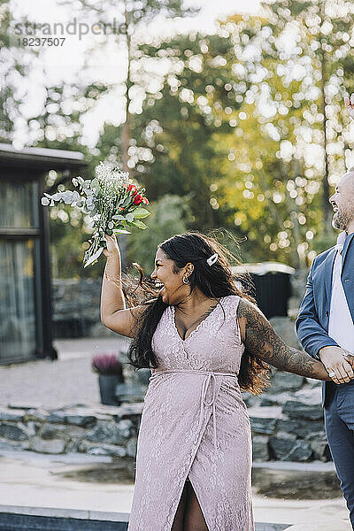 Fröhliche junge Braut mit Blumenstrauß und Bräutigam bei der Hochzeit