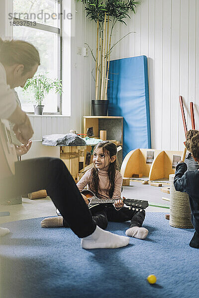 Mädchen lernt Gitarre von männlichem Kinderbetreuer im Kindergarten
