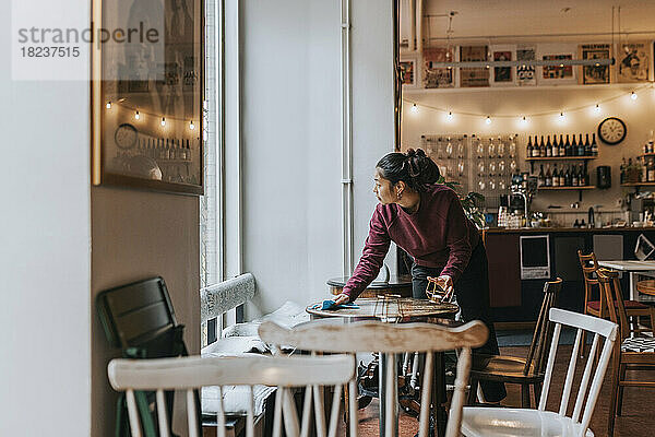 Unternehmerin reinigt Tisch mit Lappen bei der Arbeit im Café
