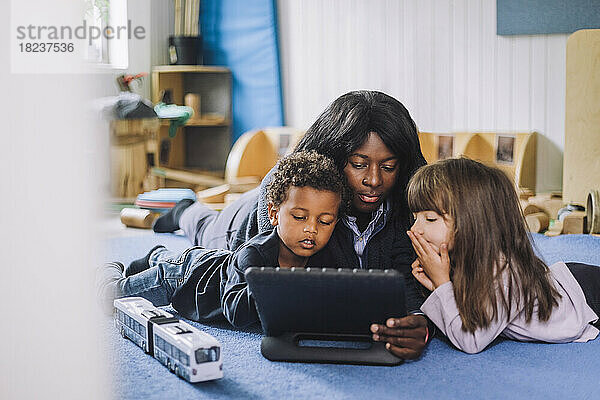 Kinderbetreuerin teilt digitales Tablet mit Schülern im Kindergarten
