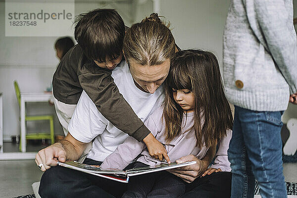 Junge  der auf ein Bilderbuch zeigt  während ein männlicher Lehrer ihm im Kindergarten eine Geschichte erzählt