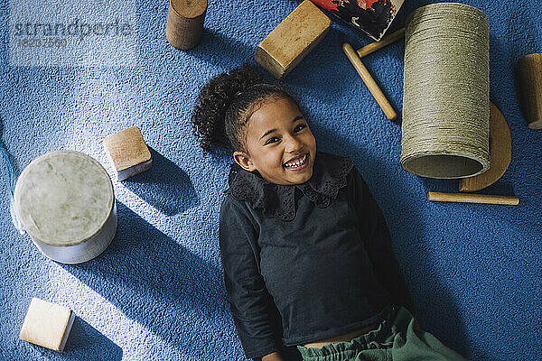 Porträt eines lächelnden Mädchens mit Spielzeug auf dem Teppich in einer Kindertagesstätte