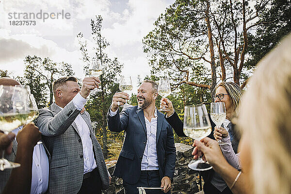 Glücklicher Bräutigam stößt mit Freunden und Familie auf der Hochzeit mit Weingläsern an