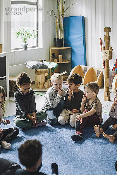 Multirassische Jungen und Mädchen mit Fingern auf den Lippen sitzen im Kindergarten