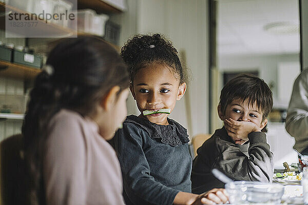 Multirassische Schülerinnen essen Gurke von männlichen Klassenkameraden in der Kindertagesstätte